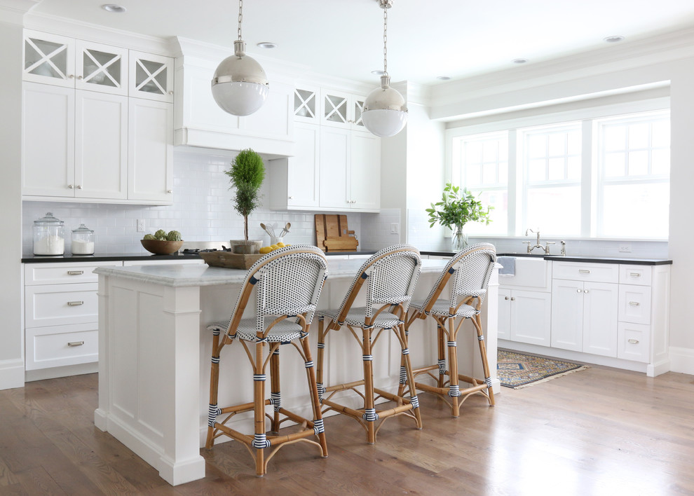Diseño de cocinas en L costera con fregadero sobremueble, armarios estilo shaker, puertas de armario blancas, salpicadero blanco, salpicadero de azulejos tipo metro, suelo de madera en tonos medios y una isla
