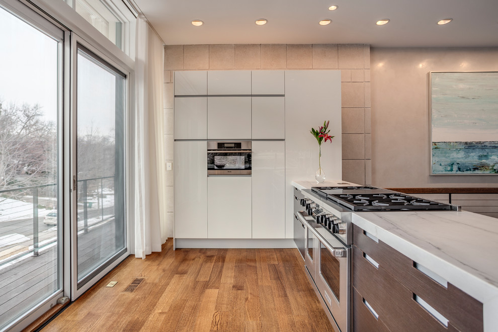 Exempel på ett modernt l-kök, med släta luckor, marmorbänkskiva, rostfria vitvaror, mellanmörkt trägolv, en köksö och brunt golv