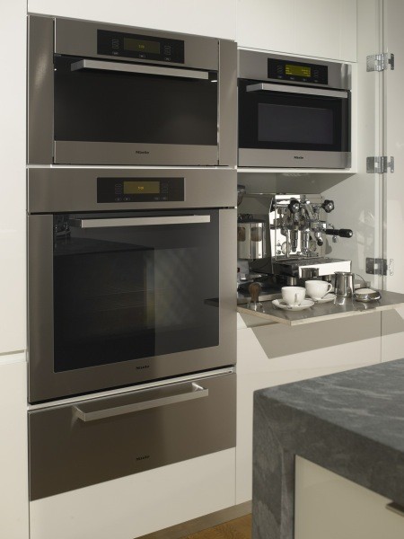 Cette photo montre une cuisine moderne de taille moyenne avec un placard à porte plane, des portes de placard blanches, une crédence blanche et un électroménager en acier inoxydable.