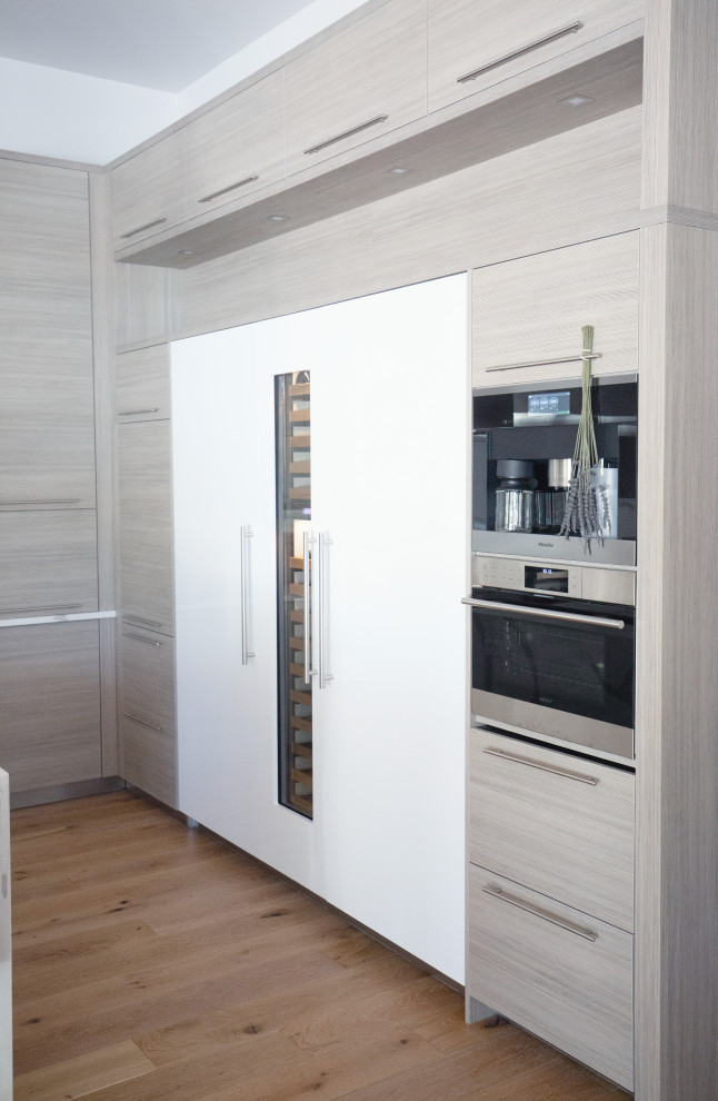 This is an example of a large beach style u-shaped kitchen/diner in Miami with a built-in sink, flat-panel cabinets, light wood cabinets, marble worktops, white splashback, marble splashback, stainless steel appliances, medium hardwood flooring, an island, brown floors and white worktops.