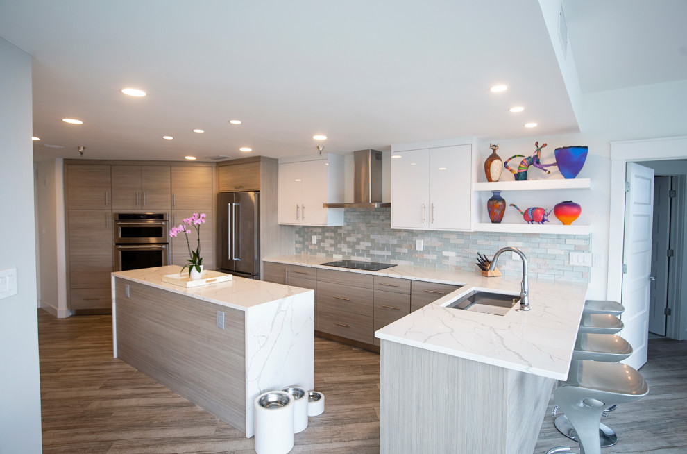 Photo of a medium sized nautical l-shaped kitchen/diner in Miami with a built-in sink, flat-panel cabinets, white cabinets, quartz worktops, white splashback, glass tiled splashback, stainless steel appliances, light hardwood flooring, an island, grey floors, white worktops and a drop ceiling.