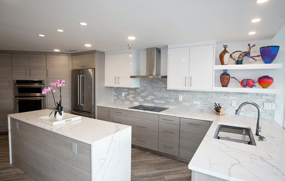 Example of a mid-sized beach style l-shaped light wood floor, gray floor and tray ceiling eat-in kitchen design in Miami with a drop-in sink, flat-panel cabinets, white cabinets, quartzite countertops, white backsplash, glass tile backsplash, stainless steel appliances, an island and white countertops