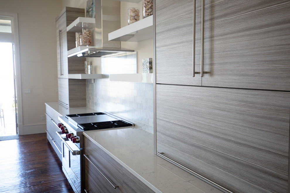 Inredning av ett maritimt stort vit linjärt vitt kök och matrum, med en nedsänkt diskho, släta luckor, skåp i ljust trä, bänkskiva i kvartsit, vitt stänkskydd, stänkskydd i cementkakel, rostfria vitvaror, mellanmörkt trägolv, en köksö och brunt golv