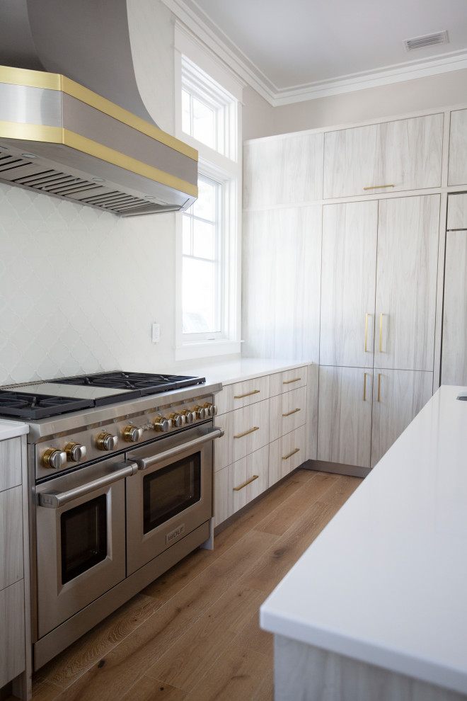 マイアミにある広いビーチスタイルのおしゃれなキッチン (ドロップインシンク、フラットパネル扉のキャビネット、淡色木目調キャビネット、珪岩カウンター、白いキッチンパネル、セラミックタイルのキッチンパネル、パネルと同色の調理設備、淡色無垢フローリング、ベージュの床、白いキッチンカウンター、折り上げ天井) の写真