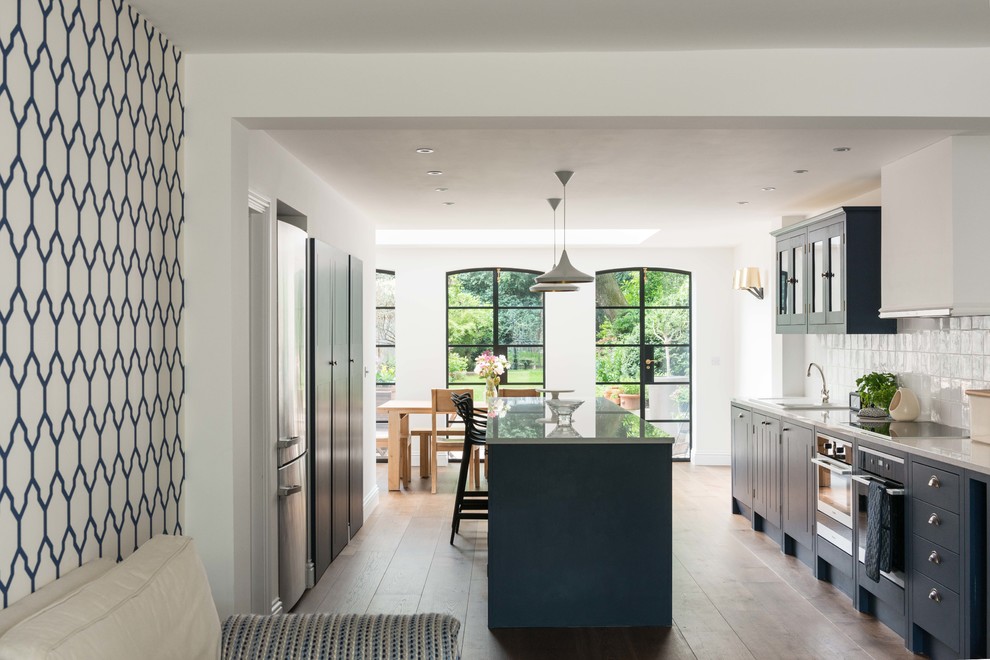 Inspiration for a mid-sized contemporary galley medium tone wood floor eat-in kitchen remodel in London with flat-panel cabinets, blue cabinets, solid surface countertops, white backsplash, cement tile backsplash, stainless steel appliances and an island