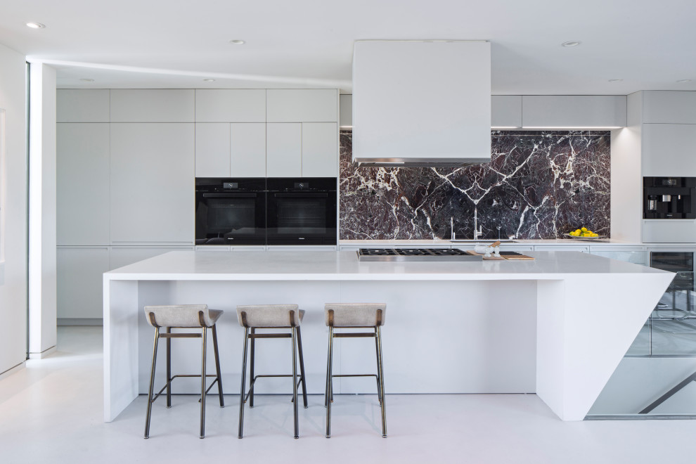 Inspiration for a contemporary galley white floor kitchen remodel in Los Angeles with flat-panel cabinets, white cabinets, gray backsplash, stone slab backsplash, black appliances, an island and white countertops