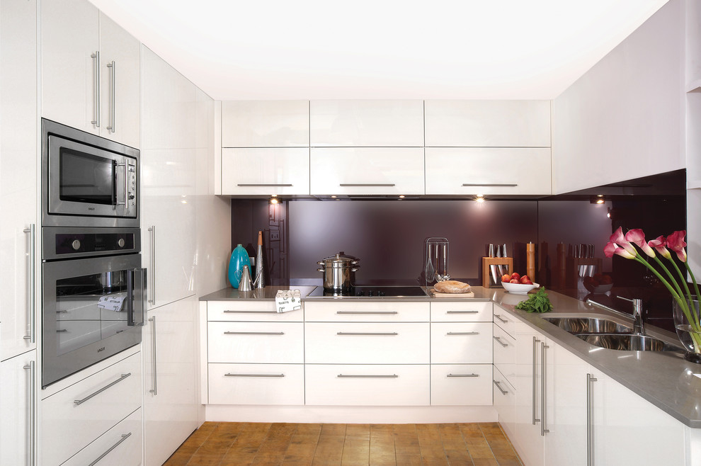 Idéer för mellanstora funkis linjära kök med öppen planlösning, med en dubbel diskho, vita skåp, bänkskiva i kvarts, rött stänkskydd, glaspanel som stänkskydd, rostfria vitvaror, mellanmörkt trägolv, en halv köksö och brunt golv