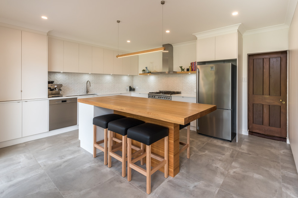 Medium sized urban l-shaped kitchen/diner in Adelaide with a submerged sink, flat-panel cabinets, white cabinets, engineered stone countertops, white splashback, mosaic tiled splashback, stainless steel appliances, cement flooring, an island, grey floors and white worktops.