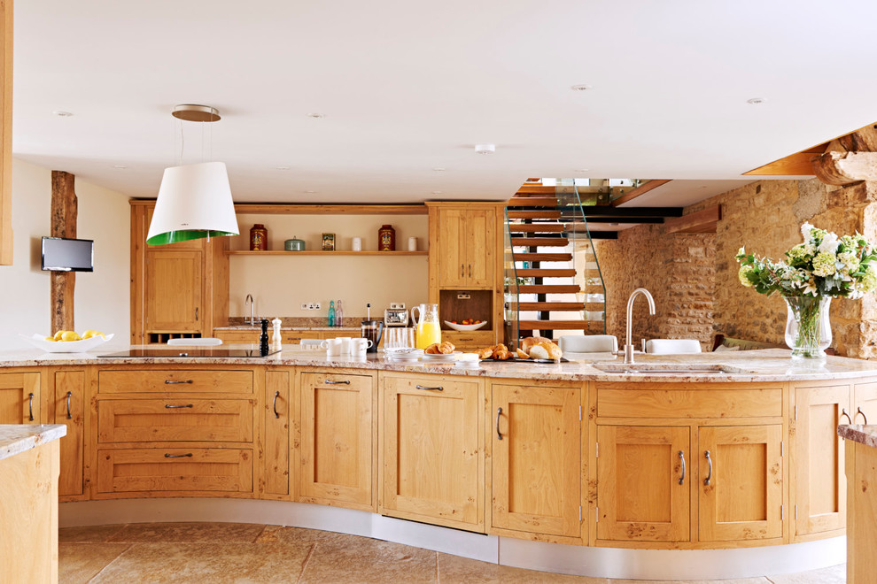 Modelo de cocina de estilo de casa de campo con fregadero bajoencimera, armarios estilo shaker, puertas de armario de madera oscura, una isla y pared de piedra
