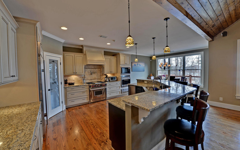 Inspiration for a large craftsman medium tone wood floor and brown floor eat-in kitchen remodel in Atlanta with an undermount sink, raised-panel cabinets, white cabinets, granite countertops, beige backsplash, travertine backsplash, stainless steel appliances and an island