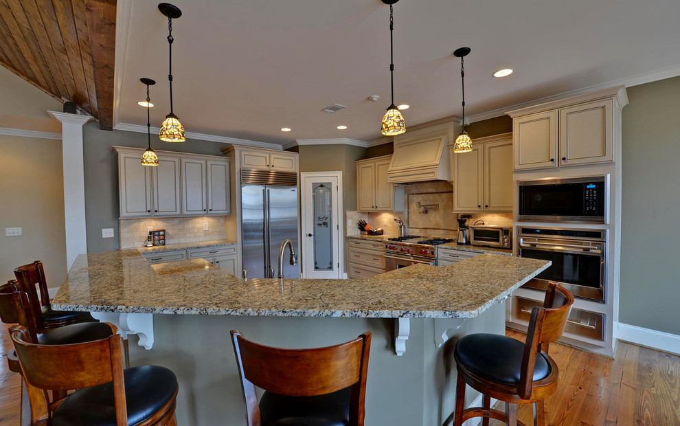 Large arts and crafts medium tone wood floor and brown floor eat-in kitchen photo in Atlanta with an undermount sink, raised-panel cabinets, white cabinets, granite countertops, beige backsplash, travertine backsplash, stainless steel appliances and an island