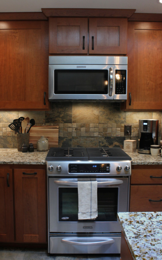 Exempel på ett amerikanskt l-kök, med en undermonterad diskho, skåp i shakerstil, skåp i mellenmörkt trä, granitbänkskiva, flerfärgad stänkskydd, stänkskydd i stenkakel, rostfria vitvaror, skiffergolv och en köksö