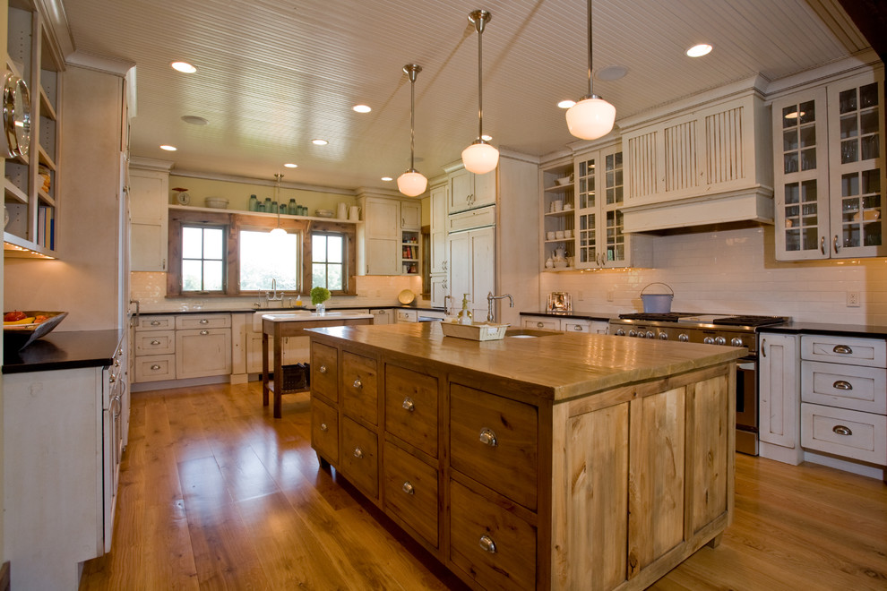 Example of a cottage kitchen design in Minneapolis with glass-front cabinets and wood countertops