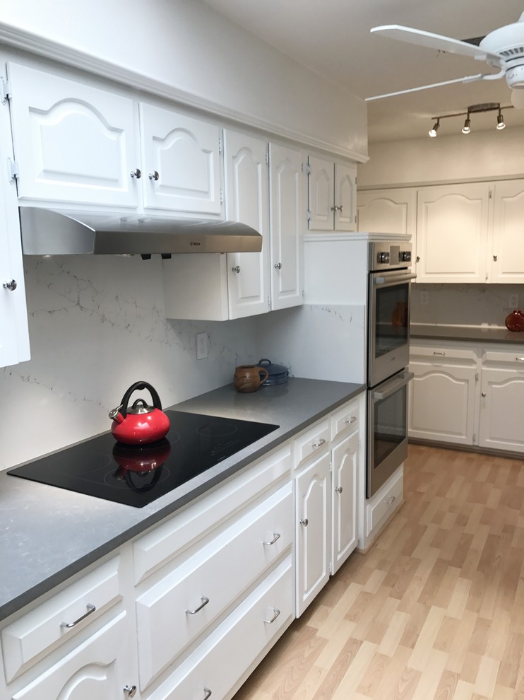 Inredning av ett amerikanskt avskilt, mellanstort u-kök, med en dubbel diskho, luckor med upphöjd panel, vita skåp, bänkskiva i kvarts, vitt stänkskydd, rostfria vitvaror och brunt golv