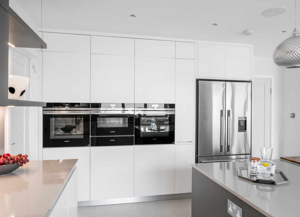 Photo of a large contemporary u-shaped kitchen/diner in London with a submerged sink, flat-panel cabinets, white cabinets, quartz worktops, grey splashback, ceramic flooring, an island, grey floors and grey worktops.