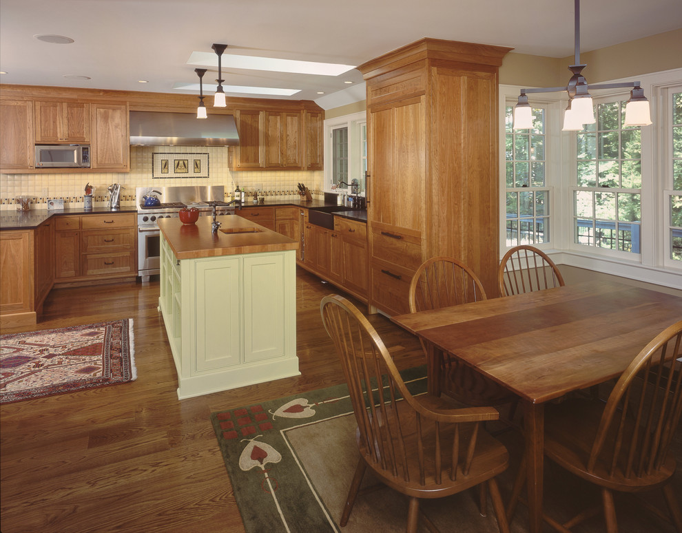 Example of a mid-sized mountain style u-shaped medium tone wood floor eat-in kitchen design in New York with wood countertops, medium tone wood cabinets, a farmhouse sink, shaker cabinets, white backsplash, porcelain backsplash, paneled appliances and an island