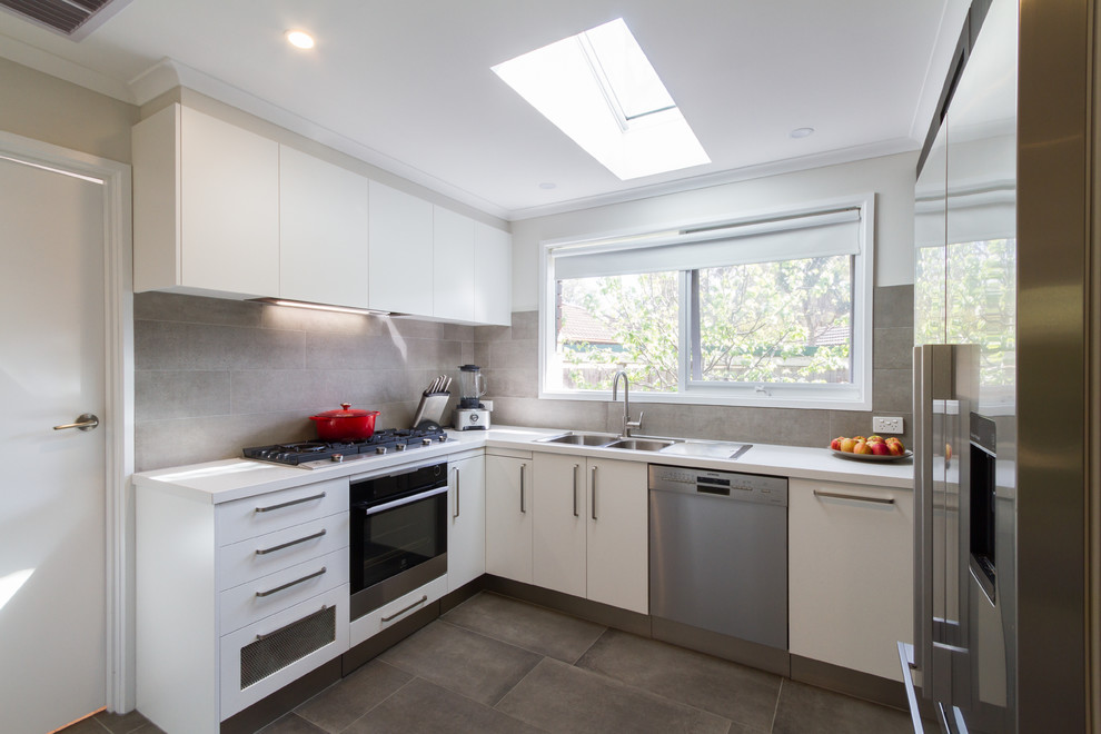 Medium sized modern u-shaped enclosed kitchen in Melbourne with a built-in sink, flat-panel cabinets, white cabinets, engineered stone countertops, grey splashback, porcelain splashback, stainless steel appliances, porcelain flooring, a breakfast bar, grey floors and white worktops.