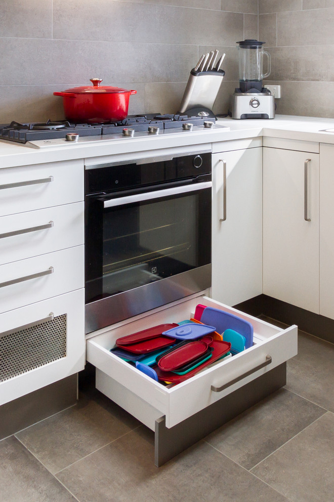 Exempel på ett avskilt, mellanstort modernt vit vitt u-kök, med en nedsänkt diskho, släta luckor, vita skåp, bänkskiva i kvarts, grått stänkskydd, stänkskydd i porslinskakel, rostfria vitvaror, klinkergolv i porslin, en halv köksö och grått golv