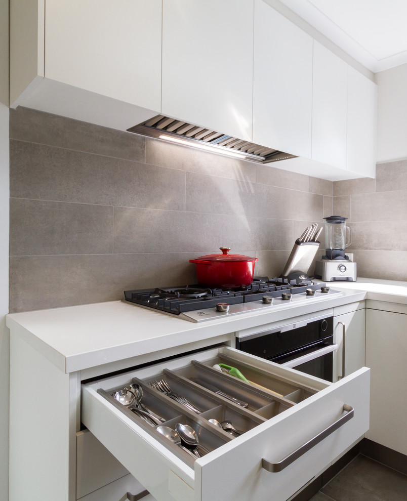 Photo of a medium sized modern u-shaped enclosed kitchen in Melbourne with a built-in sink, flat-panel cabinets, white cabinets, engineered stone countertops, grey splashback, porcelain splashback, stainless steel appliances, porcelain flooring, a breakfast bar, grey floors and white worktops.