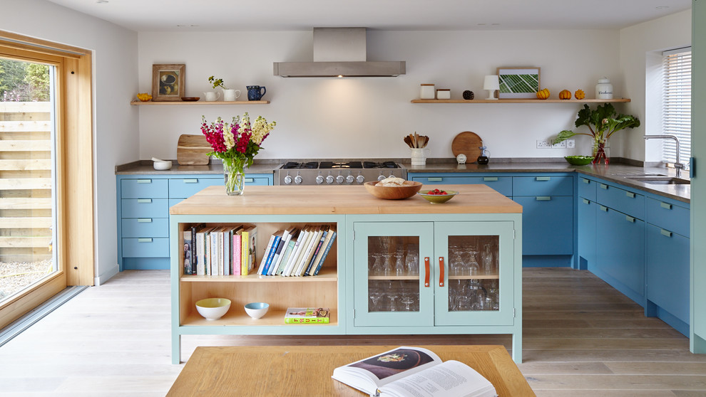 Nordische Küche in L-Form mit flächenbündigen Schrankfronten, blauen Schränken, Küchengeräten aus Edelstahl, hellem Holzboden und Kücheninsel in Wiltshire