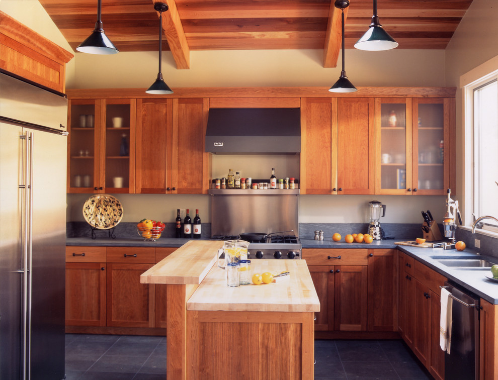 Foto på ett amerikanskt kök, med rostfria vitvaror, en undermonterad diskho, skåp i shakerstil, skåp i mellenmörkt trä, bänkskiva i täljsten och grått golv
