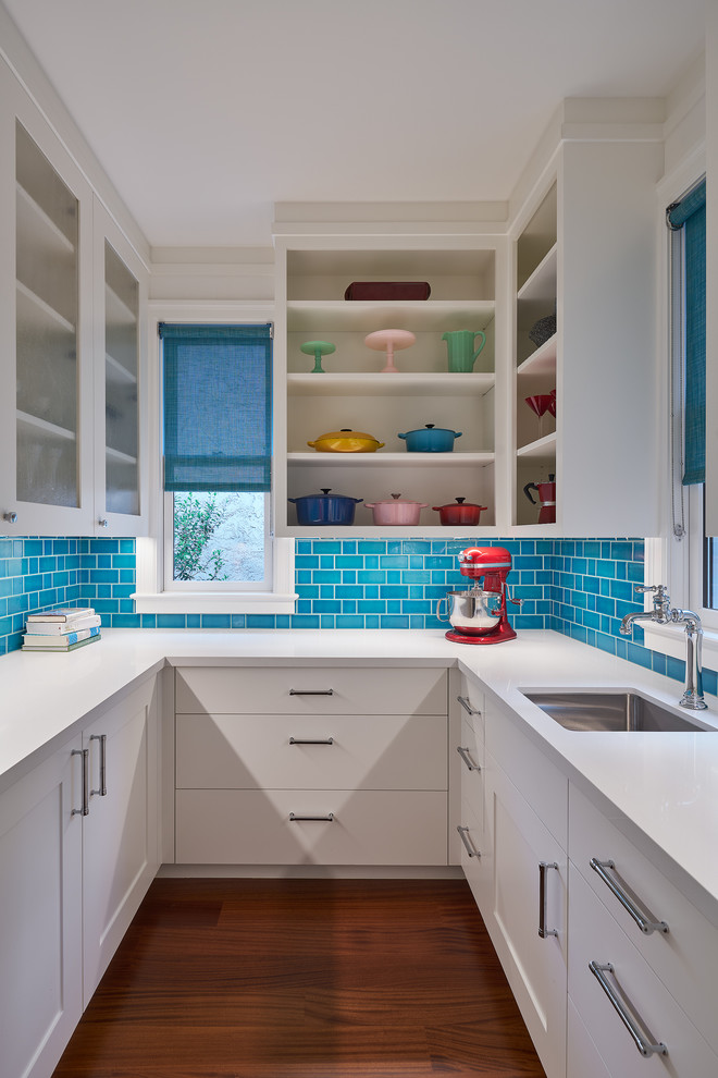 Design ideas for a medium sized contemporary u-shaped kitchen pantry in San Francisco with a submerged sink, open cabinets, white cabinets, blue splashback, metro tiled splashback, medium hardwood flooring, white worktops, composite countertops and brown floors.