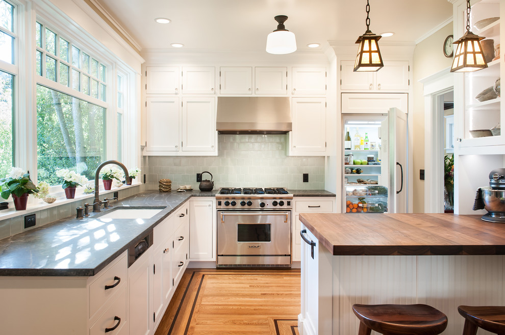 Bild på ett litet vintage kök, med en enkel diskho, luckor med profilerade fronter, vita skåp, bänkskiva i täljsten, grönt stänkskydd, stänkskydd i keramik, vita vitvaror, ljust trägolv och en köksö