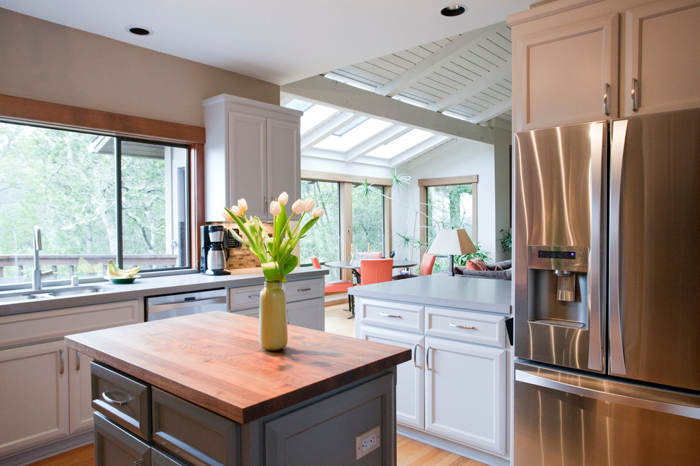 Example of a mid-sized transitional u-shaped medium tone wood floor kitchen design in San Francisco with an undermount sink, recessed-panel cabinets, white cabinets, limestone countertops, brown backsplash, glass sheet backsplash, stainless steel appliances and an island