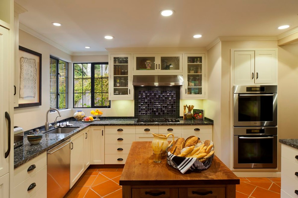 Exempel på ett klassiskt kök, med luckor med glaspanel, rostfria vitvaror, träbänkskiva och beige skåp
