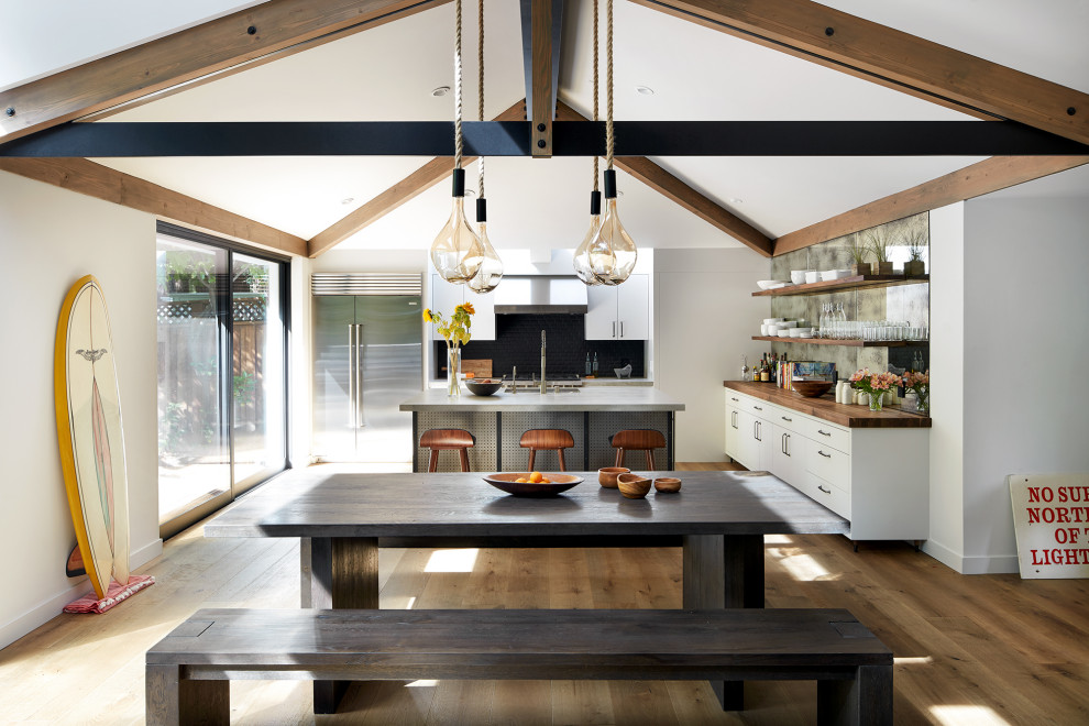 Inspiration for a coastal medium tone wood floor, exposed beam and vaulted ceiling eat-in kitchen remodel in San Francisco with flat-panel cabinets, white cabinets, black backsplash, stainless steel appliances, an island and gray countertops