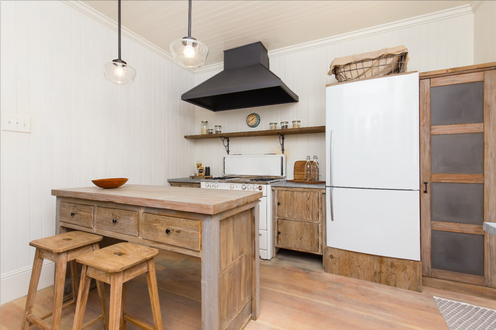 Photo of a small rustic enclosed kitchen in San Francisco with a belfast sink, medium wood cabinets, white splashback, wood splashback, white appliances, light hardwood flooring and an island.