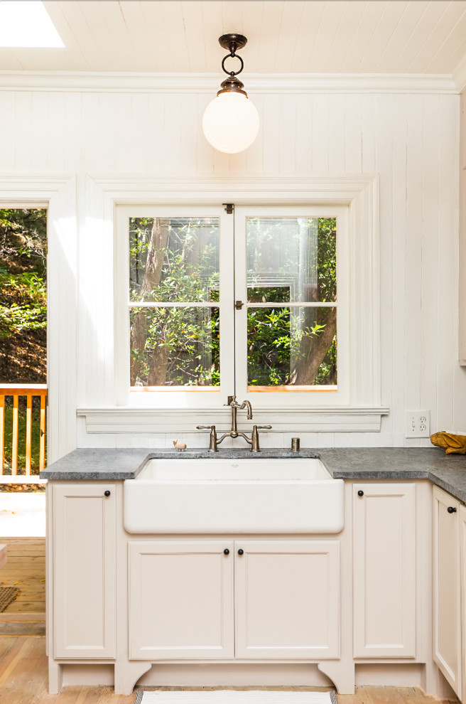 Cette image montre une petite cuisine chalet en bois brun fermée avec un évier de ferme, une crédence blanche, une crédence en bois, un électroménager blanc, parquet clair et îlot.