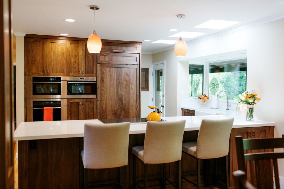 Large classic l-shaped kitchen/diner in Seattle with a belfast sink, shaker cabinets, dark wood cabinets, composite countertops, stainless steel appliances, dark hardwood flooring, an island and brown floors.