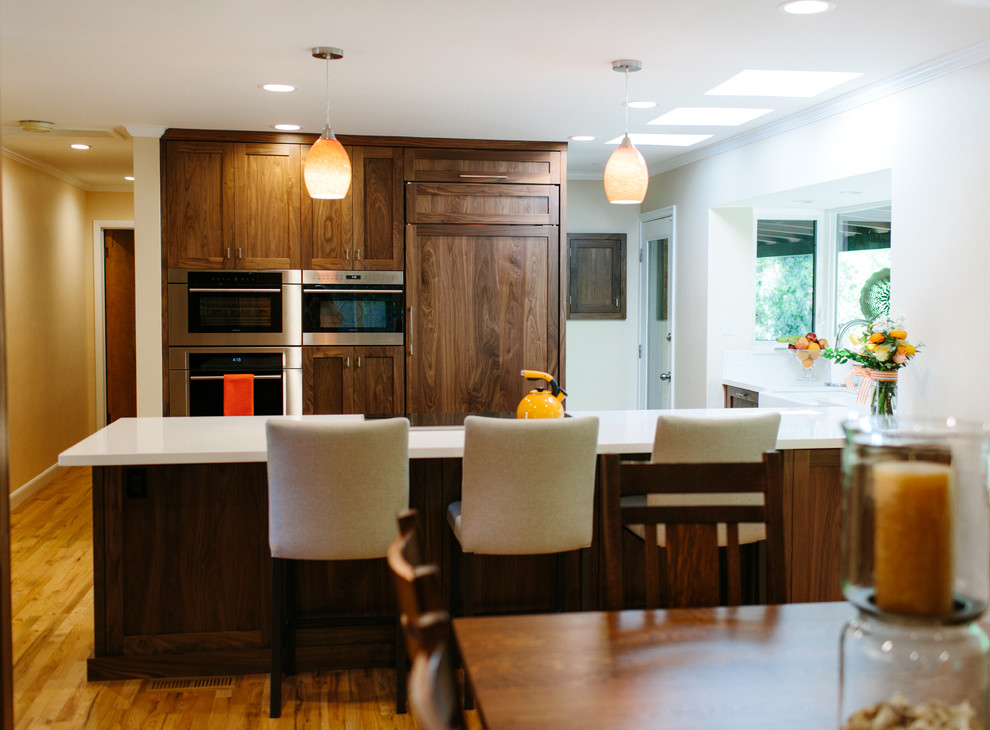 Design ideas for a large traditional l-shaped kitchen/diner in Seattle with a belfast sink, shaker cabinets, dark wood cabinets, composite countertops, stainless steel appliances, dark hardwood flooring, an island and brown floors.