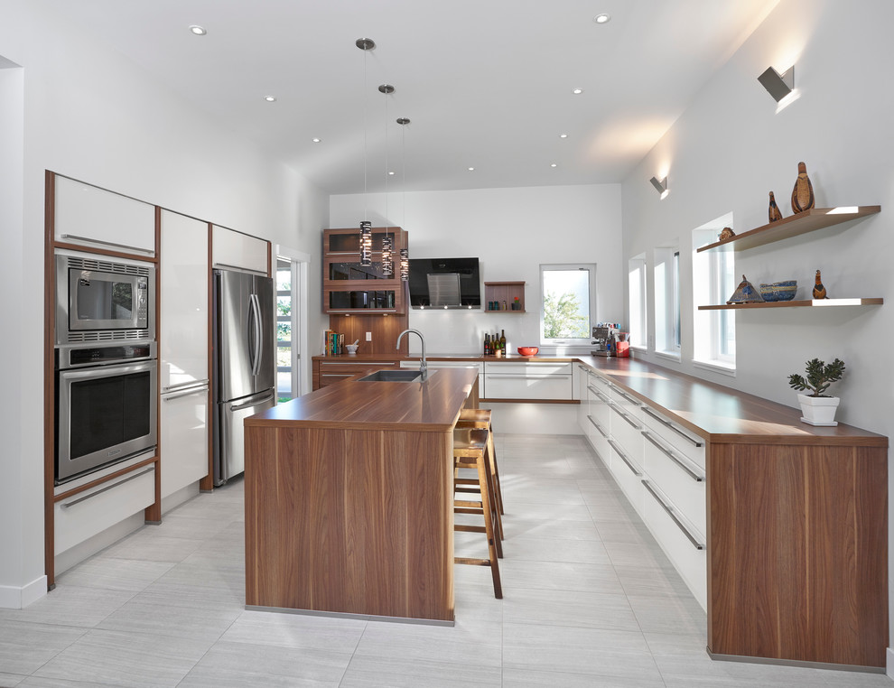 Design ideas for a large contemporary u-shaped kitchen/diner in Edmonton with a submerged sink, flat-panel cabinets, white cabinets, wood worktops, stainless steel appliances, ceramic flooring, an island, white splashback and grey floors.