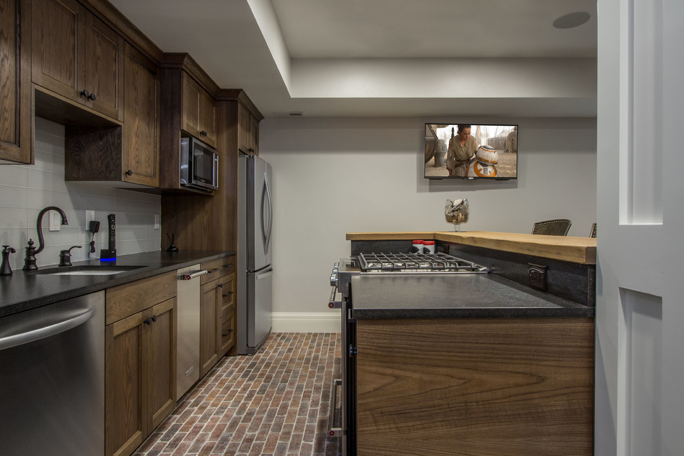 Example of a mid-sized cottage single-wall brick floor and red floor kitchen design in Salt Lake City with an undermount sink, recessed-panel cabinets, dark wood cabinets, quartz countertops, gray backsplash, glass tile backsplash, stainless steel appliances, a peninsula and black countertops