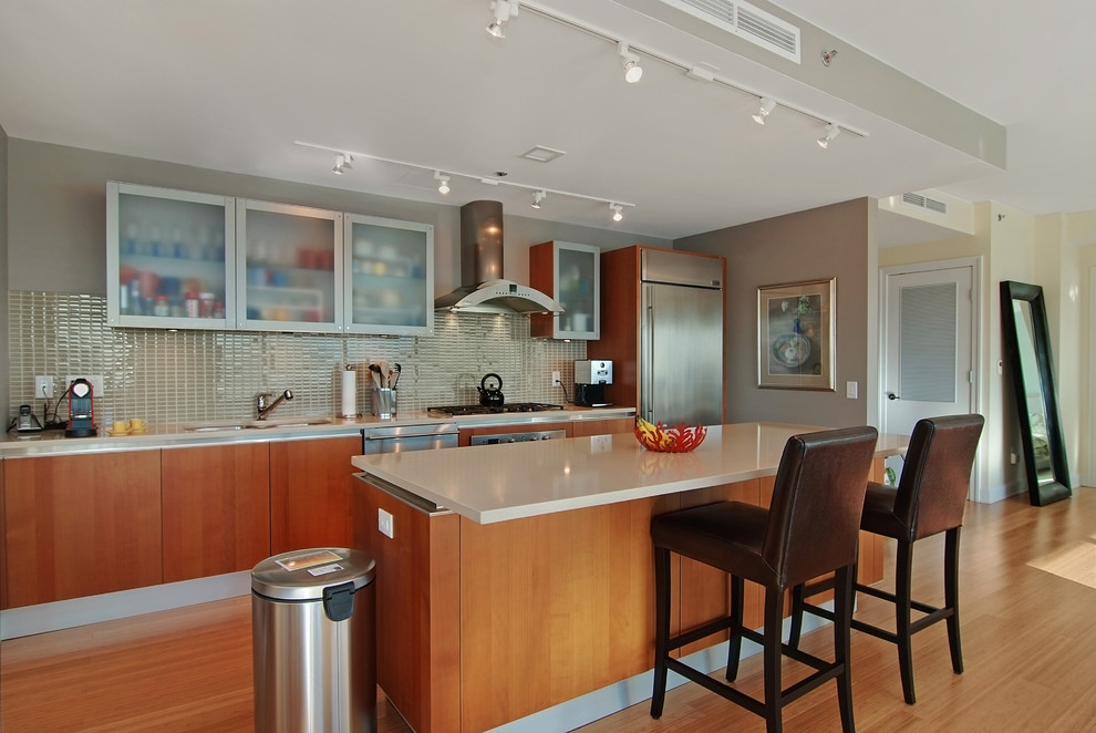 Example of a mid-sized trendy single-wall light wood floor eat-in kitchen design in Chicago with glass-front cabinets, stainless steel appliances, an undermount sink, medium tone wood cabinets, beige backsplash, ceramic backsplash, an island and quartz countertops
