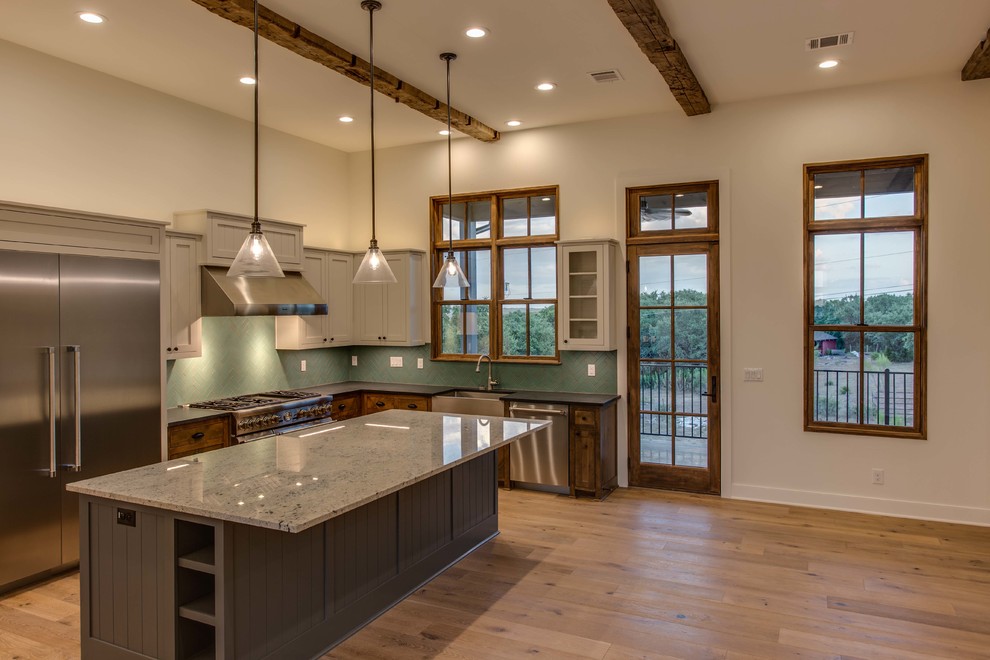 Example of a mid-sized transitional l-shaped light wood floor and beige floor open concept kitchen design in Austin with a farmhouse sink, blue backsplash, stainless steel appliances, an island, shaker cabinets, gray cabinets, granite countertops and gray countertops