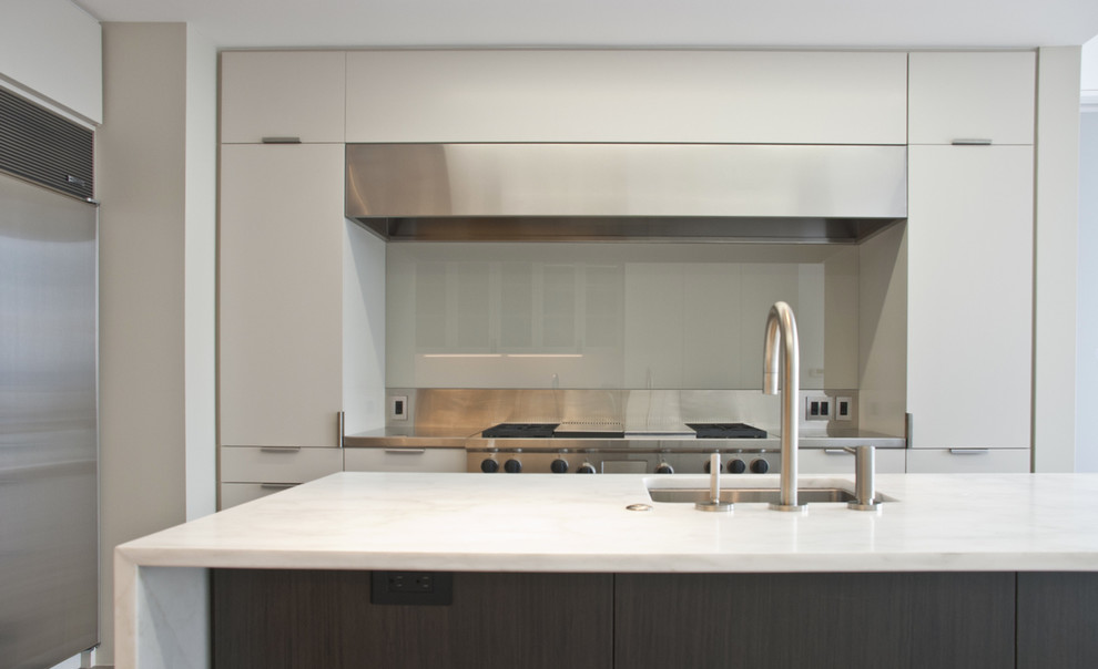 This is an example of a large modern enclosed kitchen in San Francisco with a submerged sink, flat-panel cabinets, white cabinets, marble worktops, stainless steel appliances, light hardwood flooring, an island and brown floors.