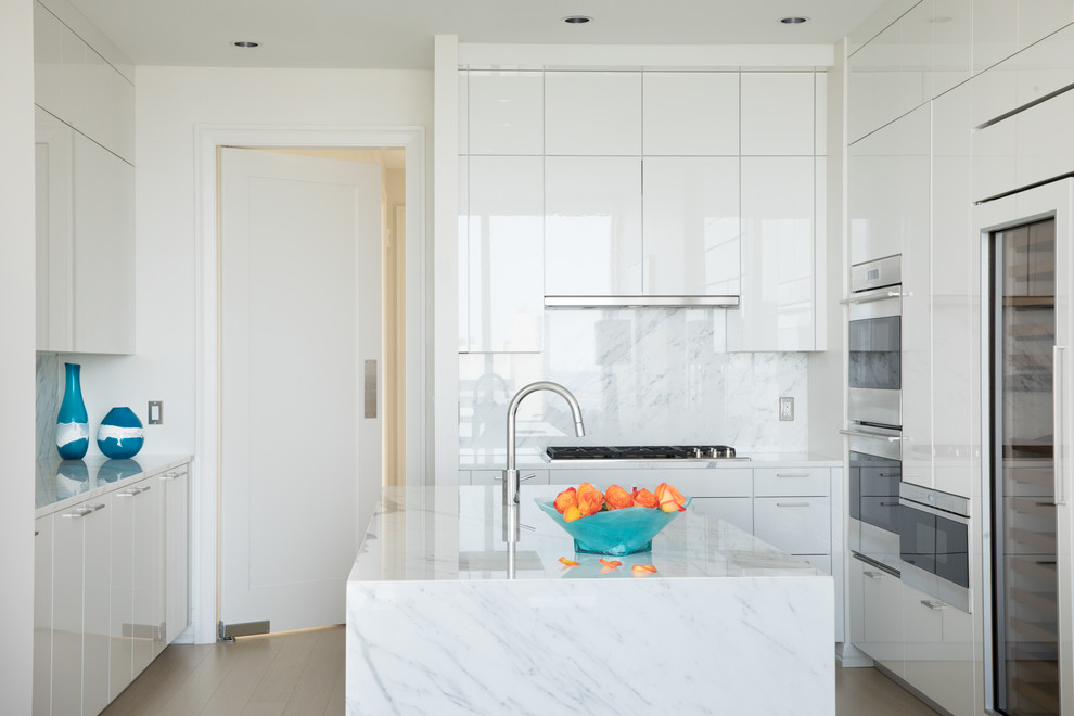 Moderne Küche in U-Form mit flächenbündigen Schrankfronten, weißen Schränken, Küchenrückwand in Weiß, Rückwand aus Stein, braunem Holzboden, Kücheninsel, braunem Boden und grauer Arbeitsplatte in Hawaii