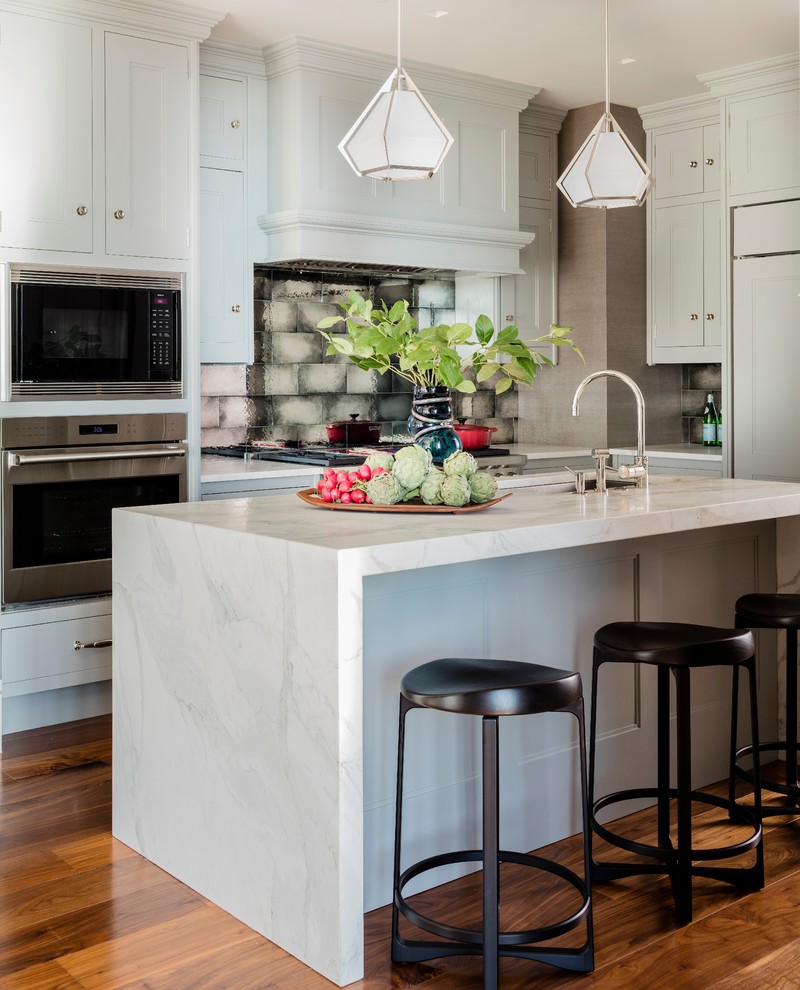 Modern inredning av ett stort kök, med en undermonterad diskho, skåp i shakerstil, grå skåp, marmorbänkskiva, grått stänkskydd, stänkskydd i glaskakel, rostfria vitvaror, mellanmörkt trägolv, en köksö och brunt golv