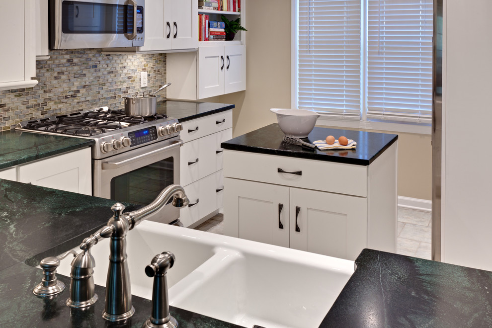 Example of a small classic u-shaped porcelain tile and beige floor eat-in kitchen design in Atlanta with stainless steel appliances, soapstone countertops, recessed-panel cabinets, white cabinets, a farmhouse sink, multicolored backsplash, glass tile backsplash, an island and green countertops