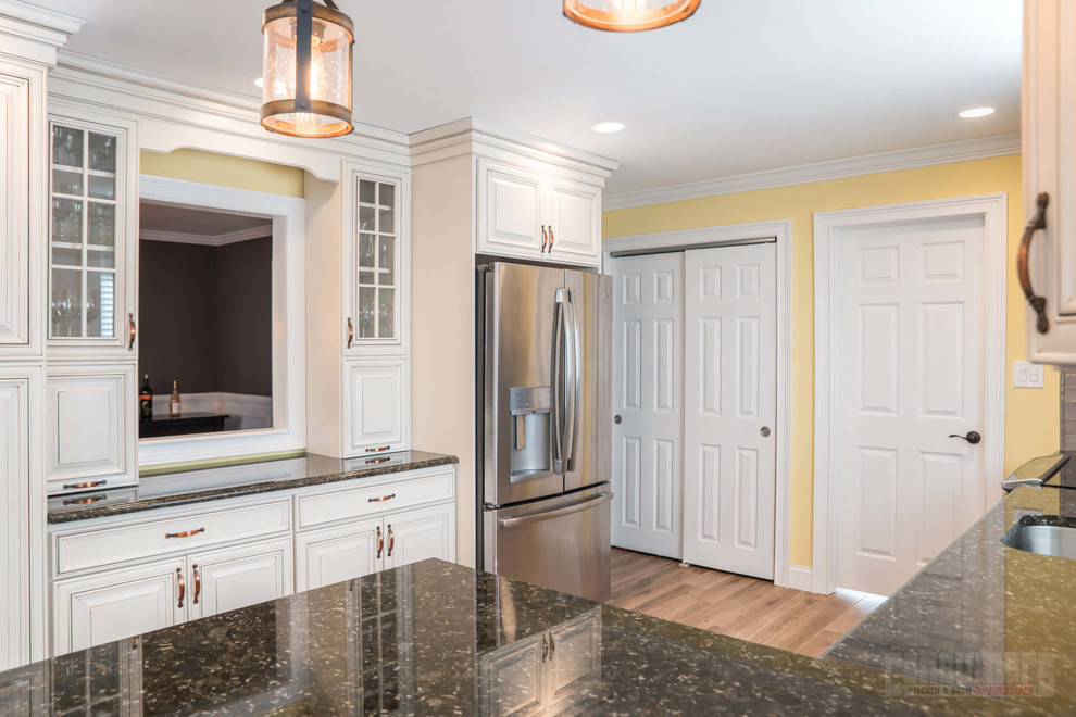 Photo of a medium sized galley kitchen/diner in New York with a submerged sink, raised-panel cabinets, yellow cabinets, granite worktops, grey splashback, cement tile splashback, stainless steel appliances, plywood flooring, a breakfast bar and beige floors.