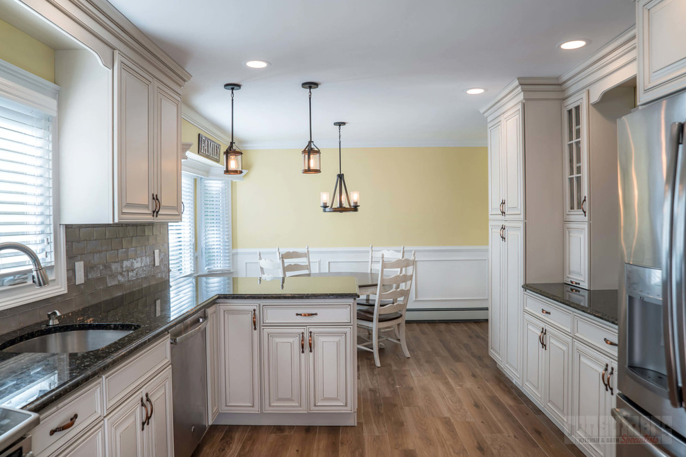 Foto på ett mellanstort kök, med en undermonterad diskho, luckor med upphöjd panel, gula skåp, granitbänkskiva, grått stänkskydd, stänkskydd i cementkakel, rostfria vitvaror, plywoodgolv, en halv köksö och beiget golv