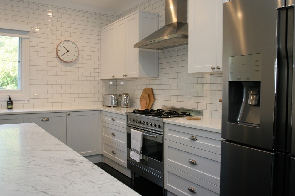 Idéer för att renovera ett stort shabby chic-inspirerat vit vitt kök, med en integrerad diskho, skåp i shakerstil, vita skåp, marmorbänkskiva, vitt stänkskydd, rostfria vitvaror, en köksö, stänkskydd i tunnelbanekakel, målat trägolv och svart golv