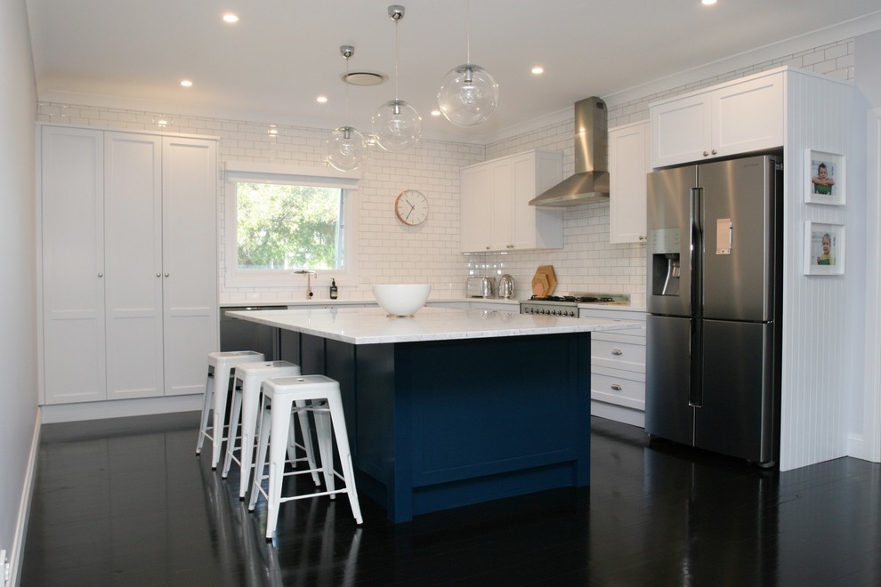 Example of a large trendy l-shaped painted wood floor and black floor open concept kitchen design in Sydney with an integrated sink, shaker cabinets, white cabinets, marble countertops, white backsplash, stainless steel appliances, an island, subway tile backsplash and white countertops