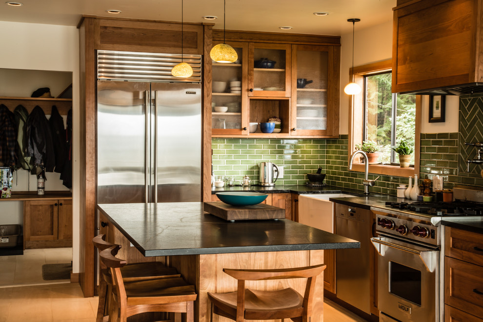 Photo of a small rural l-shaped kitchen/diner in Vancouver with a belfast sink, shaker cabinets, medium wood cabinets, soapstone worktops, green splashback, metro tiled splashback, stainless steel appliances, an island, porcelain flooring and beige floors.
