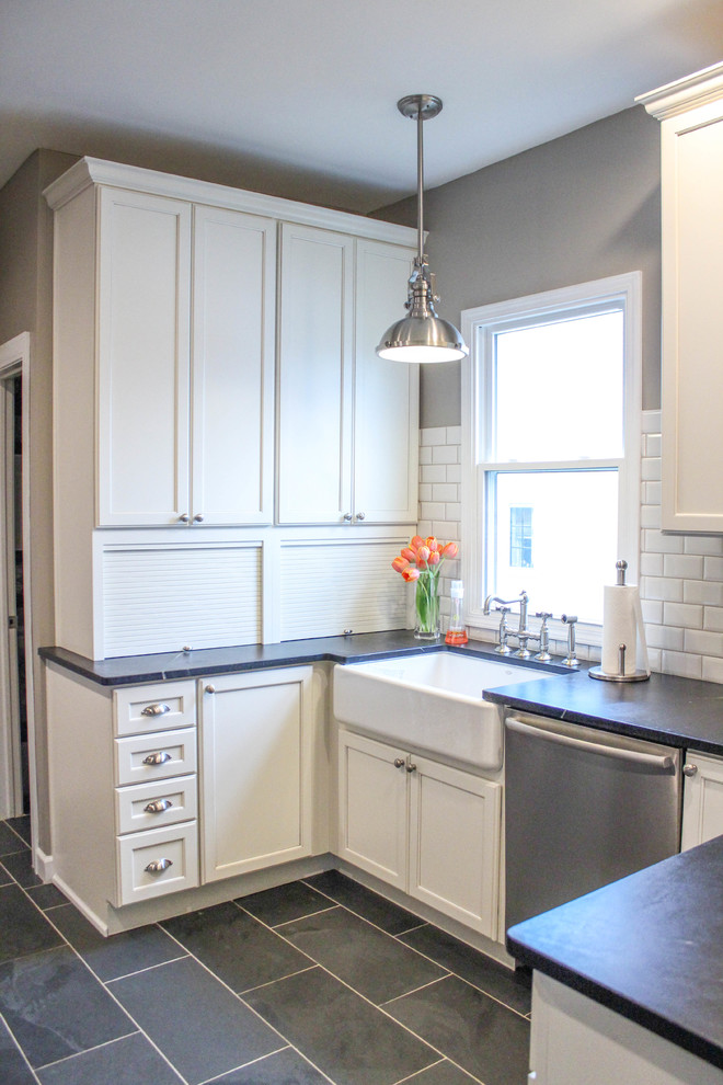 Foto på ett litet lantligt kök, med en rustik diskho, luckor med infälld panel, vita skåp, bänkskiva i täljsten, vitt stänkskydd, stänkskydd i tunnelbanekakel och rostfria vitvaror