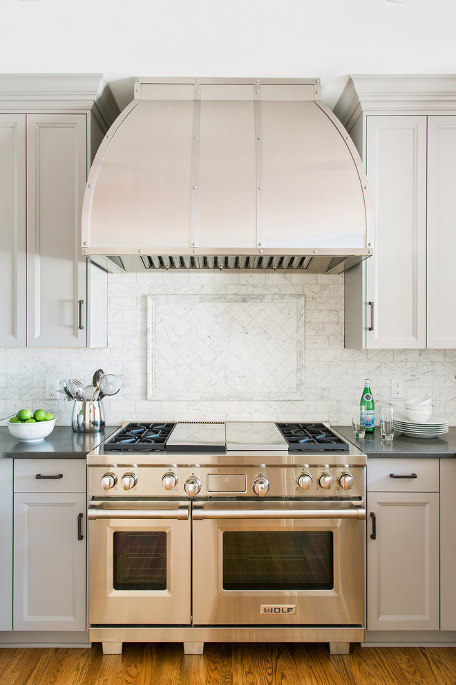 Inspiration for a mid-sized transitional u-shaped medium tone wood floor enclosed kitchen remodel in Atlanta with an undermount sink, recessed-panel cabinets, gray cabinets, quartz countertops, white backsplash, stone tile backsplash, stainless steel appliances and a peninsula