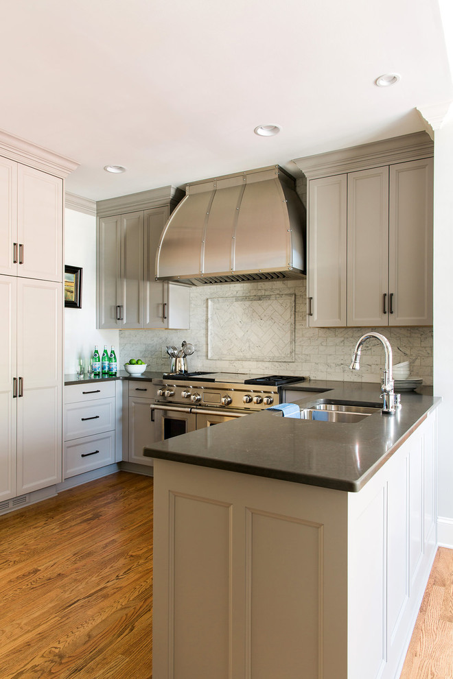 Klassisk inredning av ett mellanstort, avskilt u-kök, med en undermonterad diskho, luckor med infälld panel, grå skåp, bänkskiva i kvarts, vitt stänkskydd, stänkskydd i stenkakel, rostfria vitvaror, mellanmörkt trägolv och en halv köksö